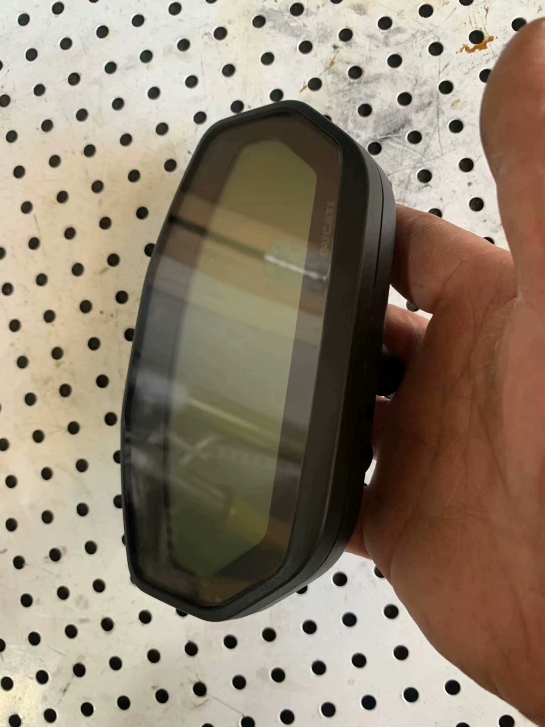 Top-angle view of Ducati Monster 797 dash display, dark LCD glass with DUCATI logo, held in hand
