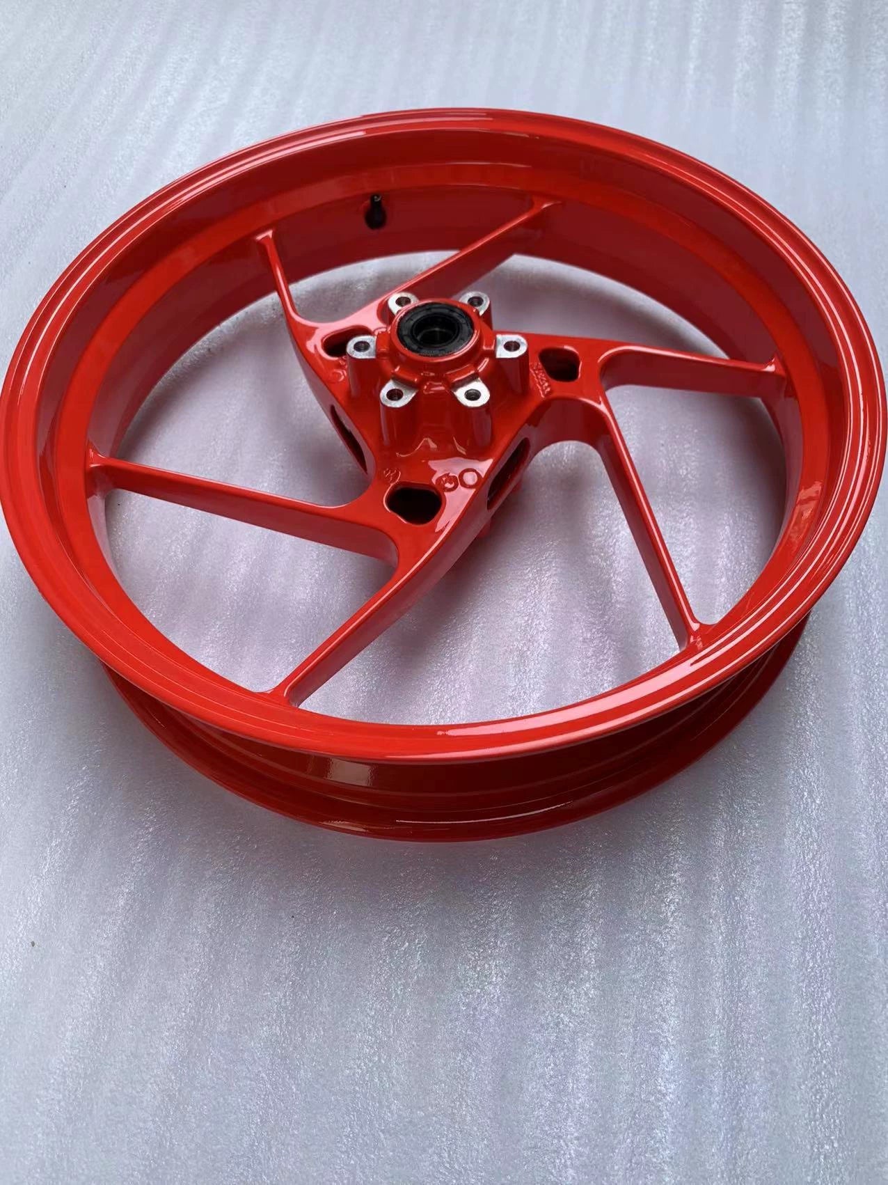Angled full view of red Aprilia RS660 front rim, five-spoke wheel with hub, glossy new condition