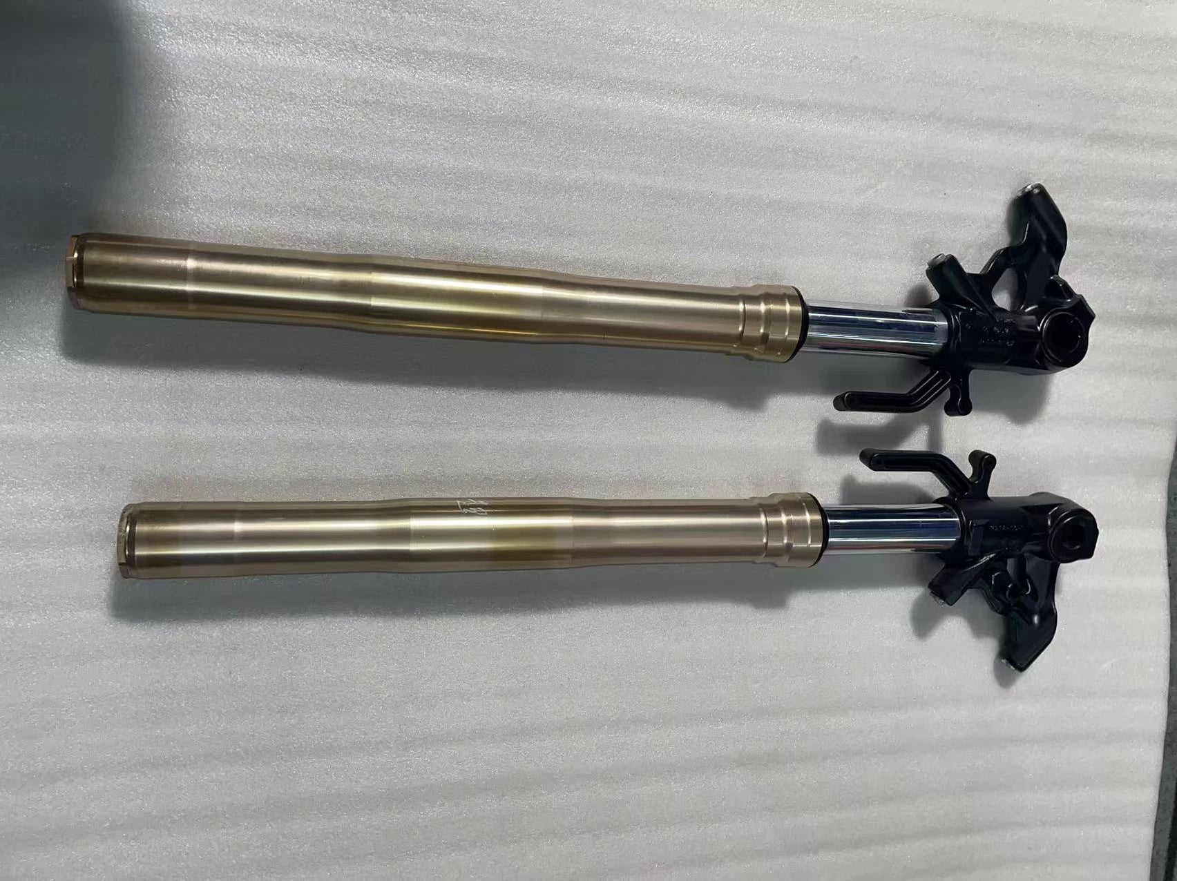Kawasaki Z1000 front fork pair laid horizontally, gold outer tubes, chrome stanchions, black lower triple clamp brackets