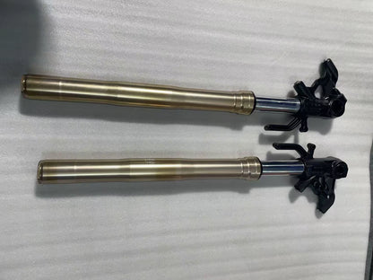 Kawasaki Z1000 front fork pair laid horizontally, gold outer tubes, chrome stanchions, black lower triple clamp brackets
