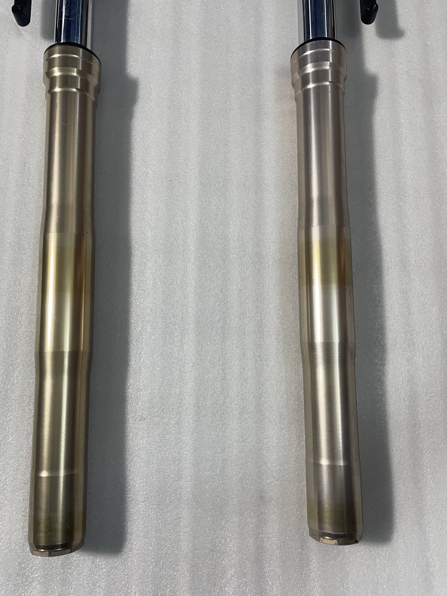 Close-up of Kawasaki Z1000 front fork gold lower tubes, showing surface finish and slight discoloration, no dents