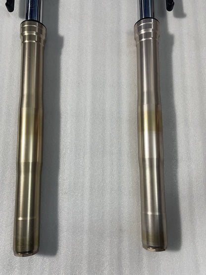Close-up of Kawasaki Z1000 front fork gold lower tubes, showing surface finish and slight discoloration, no dents