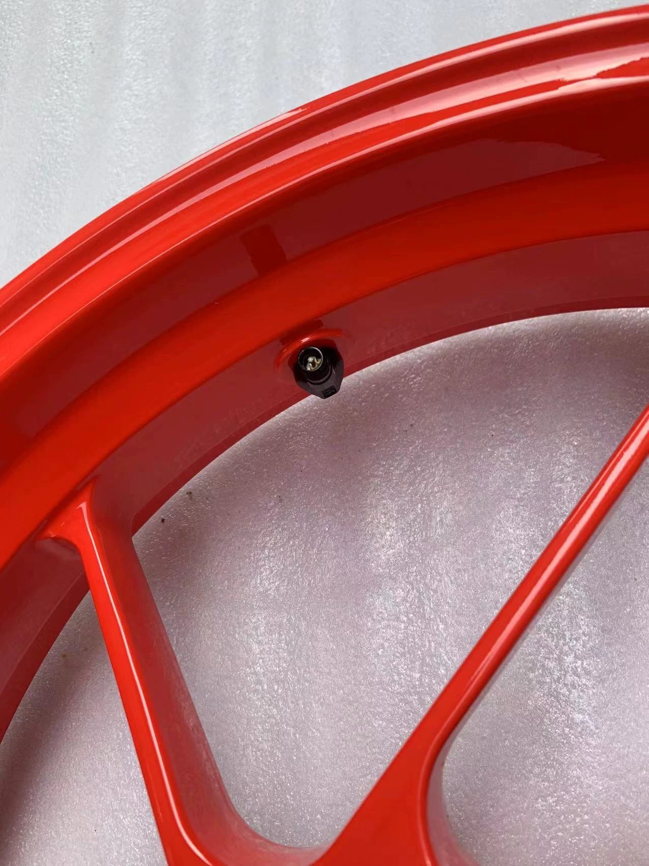 Close-up of red RS660 front rim edge and black tire valve stem, glossy paint condition