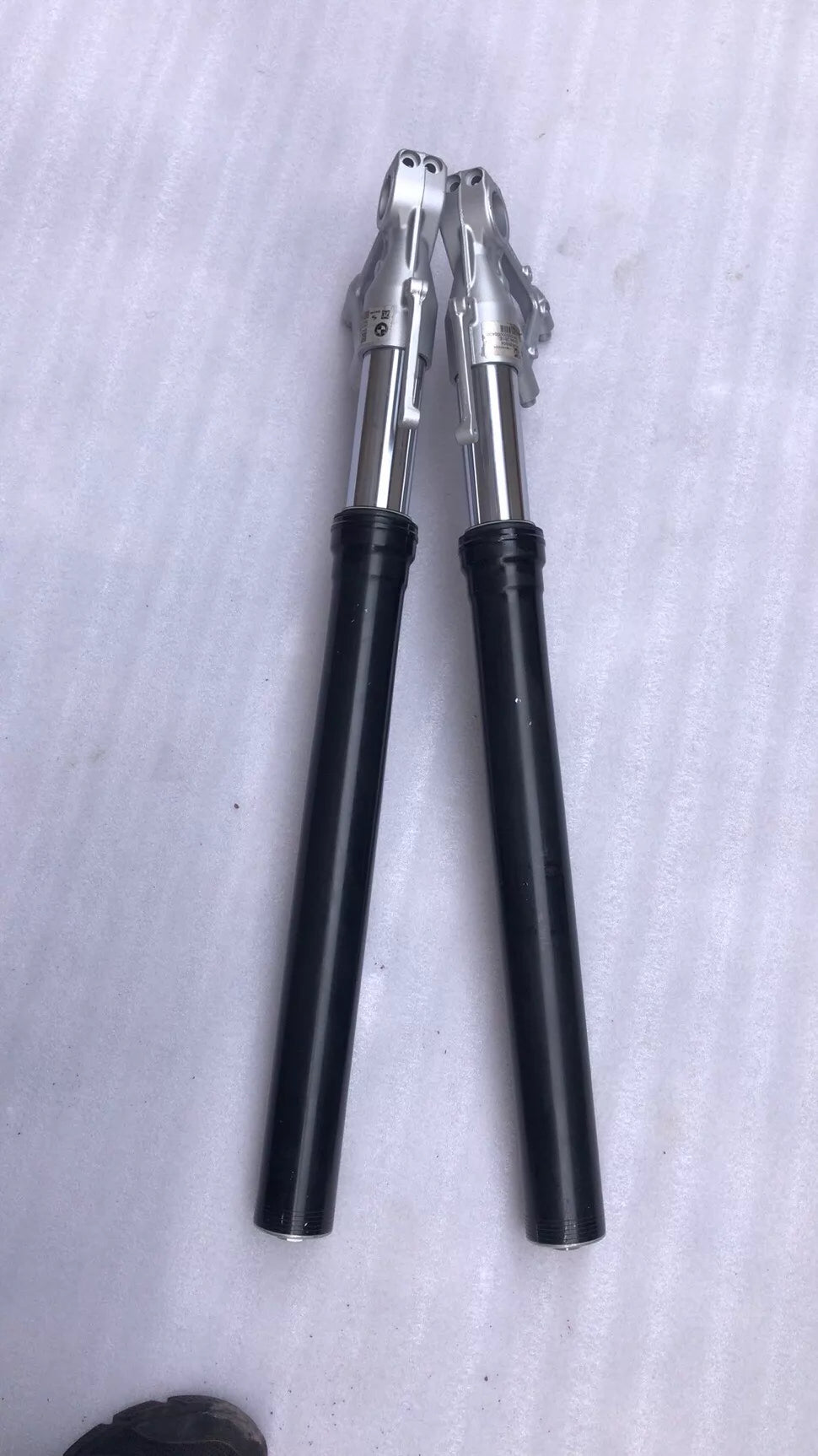 BMW S1000R fork leg pair laid flat, bottom view revealing axle holes and lower leg casting