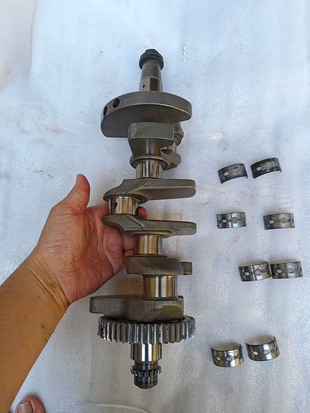 Full vertical Yamaha MT-09 crankshaft held in hand with primary drive gear at base and six loose main bearing shells