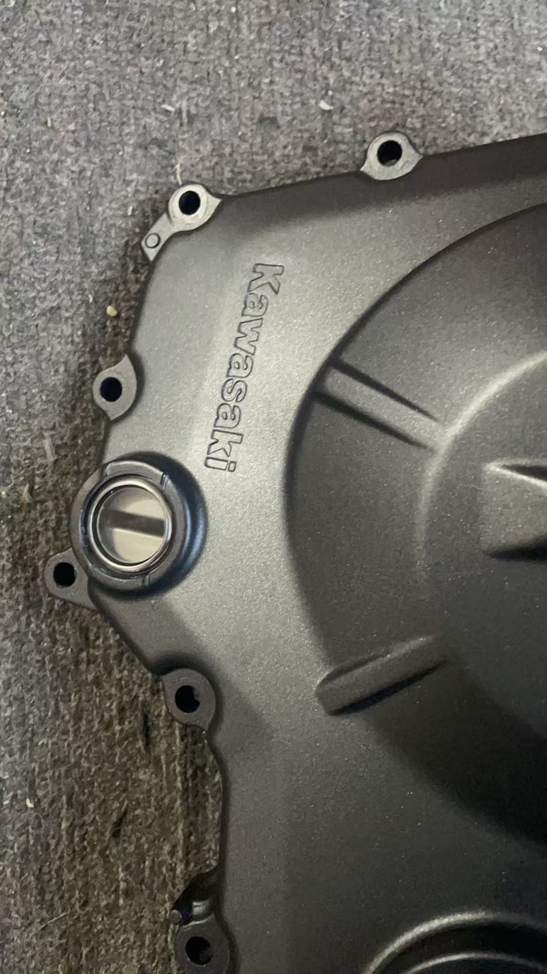 Close-up of Kawasaki logo and inspection cap on ZX-4R clutch cover, matte black finish, minor wear