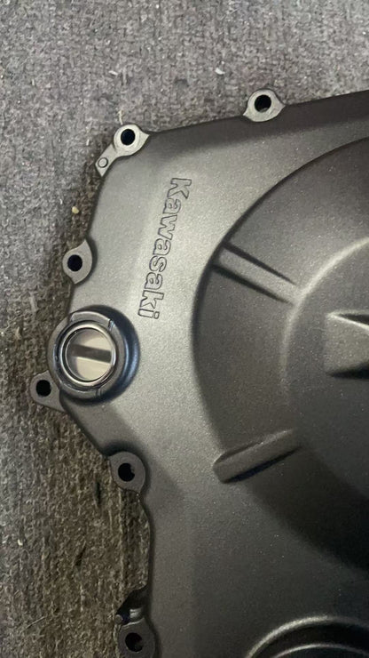Close-up of Kawasaki logo and inspection cap on ZX-4R clutch cover, matte black finish, minor wear