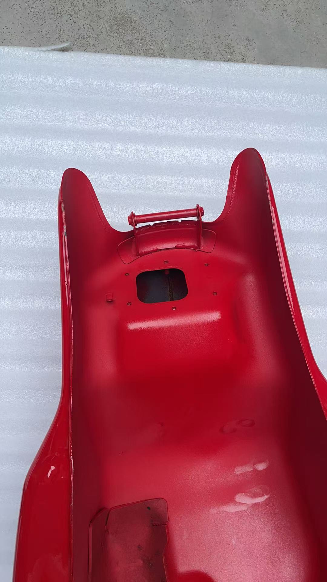 Underside rear view of red Ducati Monster 821 tank showing mounting bracket, holes and fuel pump cutout