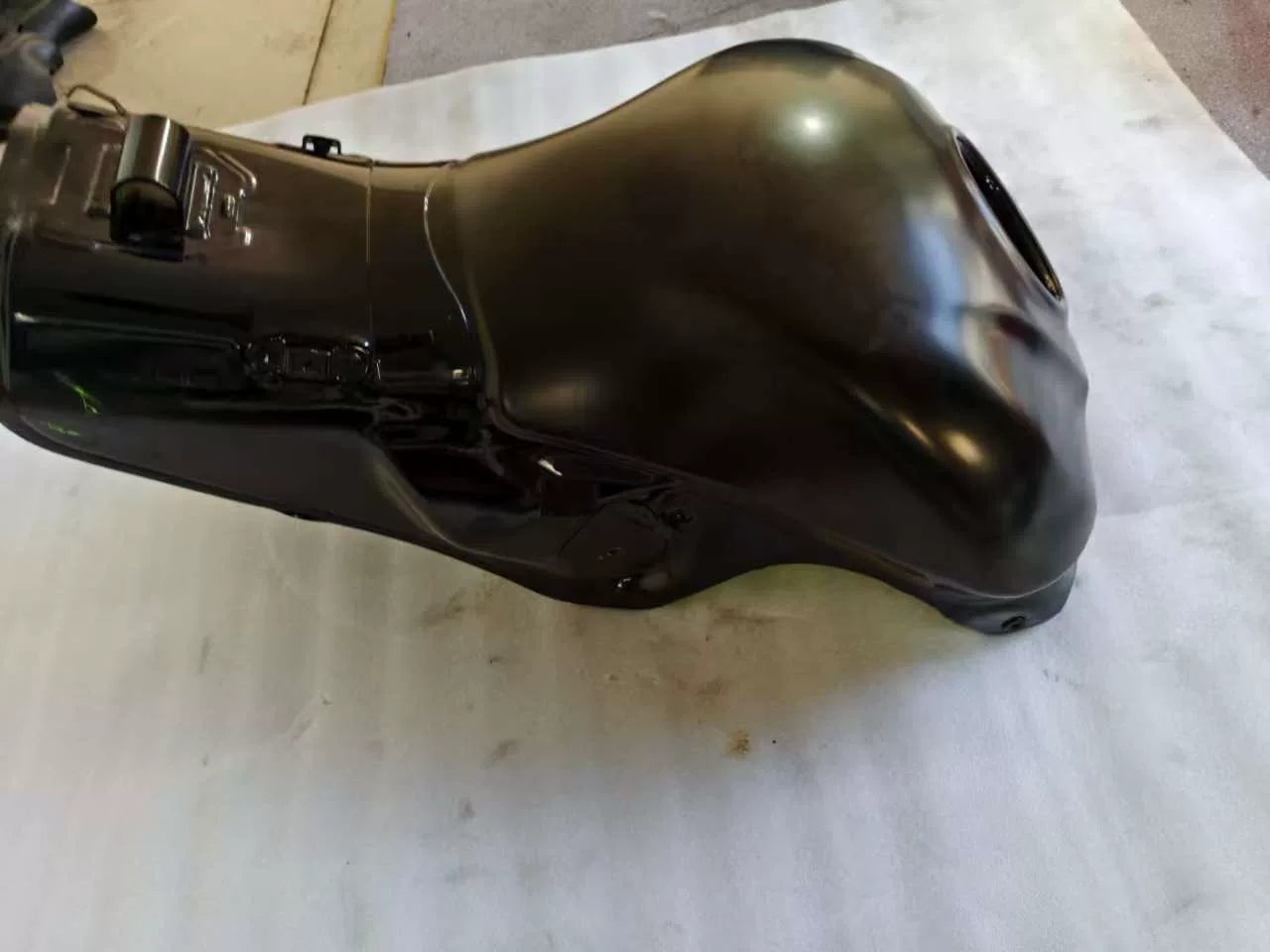 Rear three-quarter side view of black Kawasaki ZX10R fuel tank, glossy paint with minor scratches near base
