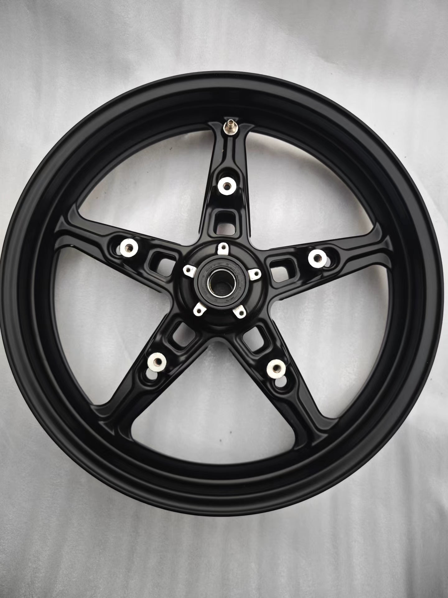 Full rear face of black 5-spoke cast front rim showing hub and valve stem, BMW R NineT