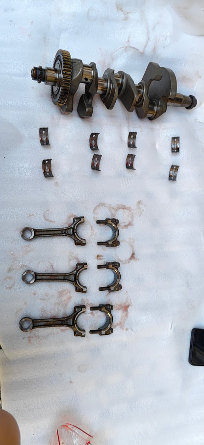 Full Yamaha MT-09 crankshaft assembly laid out with main bearing shells and three connecting rods with caps on white sheet