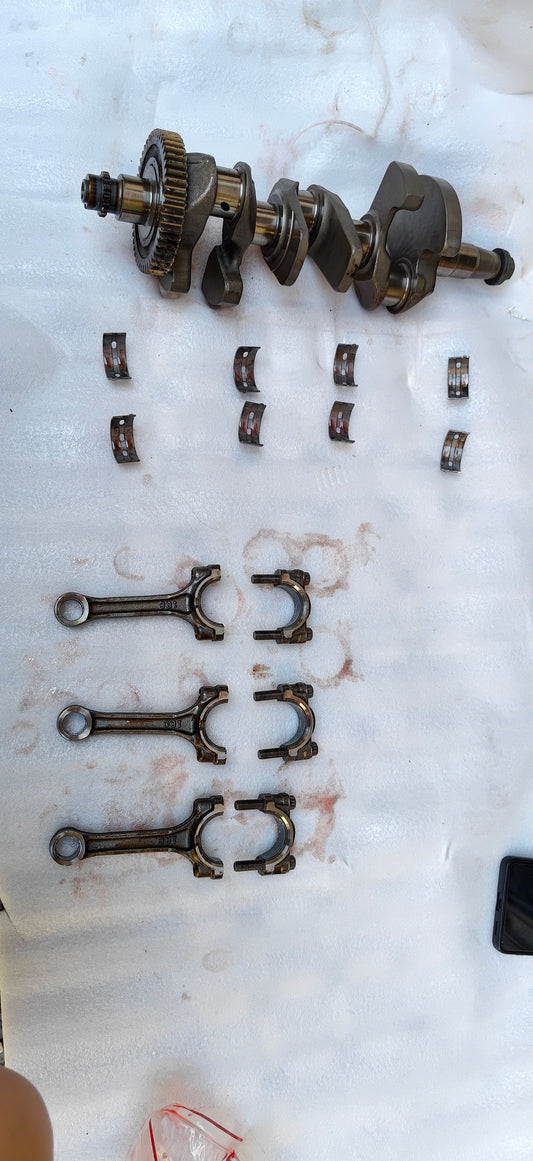 Full Yamaha MT-09 crankshaft assembly laid out with main bearing shells and three connecting rods with caps on white sheet