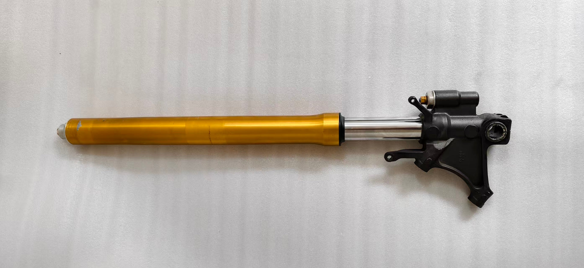 Single Yamaha YZF-R6 front fork laid horizontally, gold upper tube, chrome slider and black axle bracket