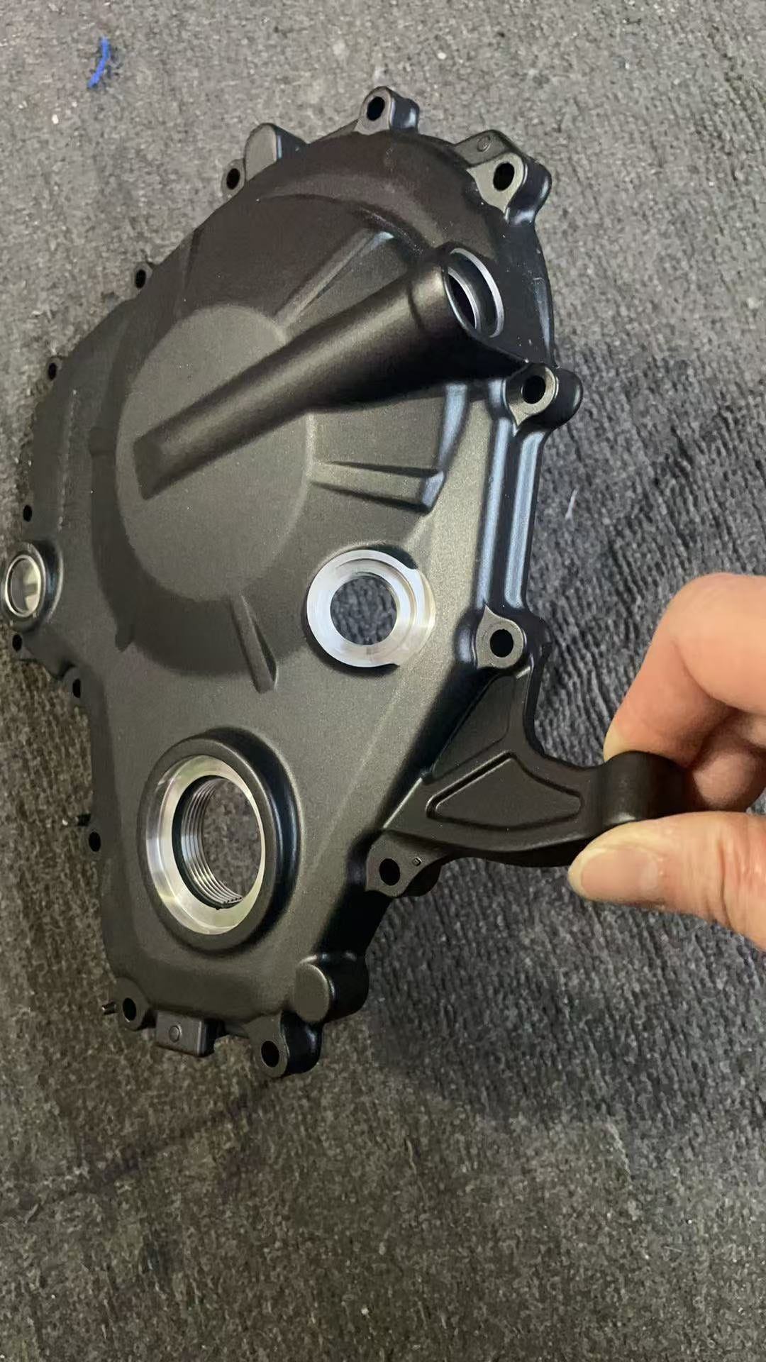 Angled outer view of ZX-4R clutch cover held in hand, showing seal bore, mounting tab and matte finish