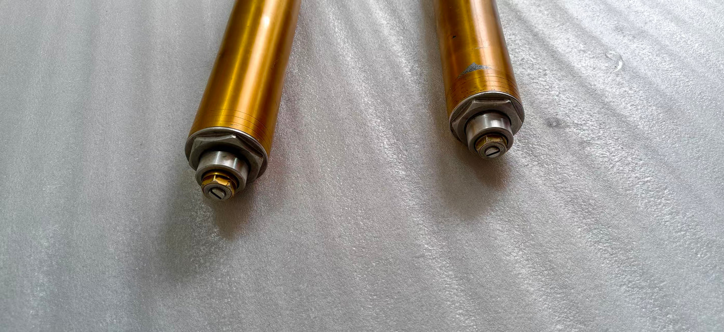Close-up of two YZF-R6 fork tube tops, gold anodized uppers with damping adjuster caps and hex fittings