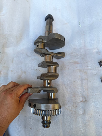 Angled full Yamaha MT-09 crankshaft held vertically, primary drive gear and splined end at bottom, tapered shaft on top